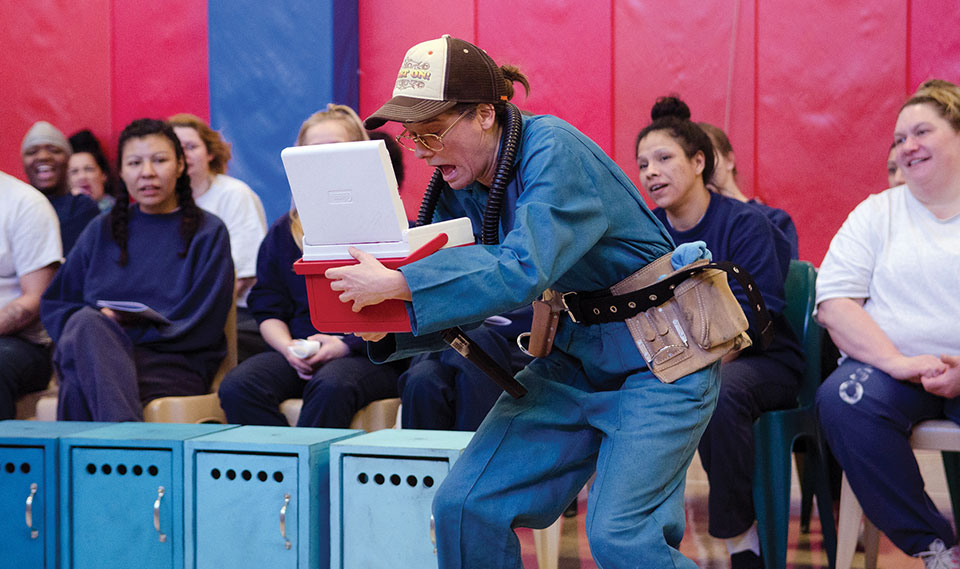 Spectators watch as an actor in costume peers inside of a mini-cooler