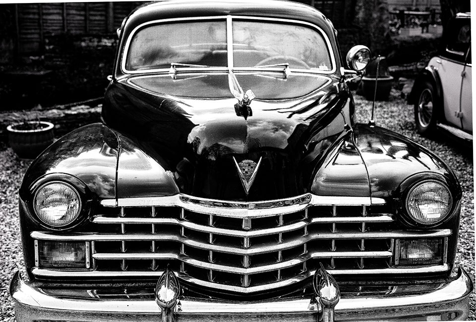 A black and white photograph of an old black Cadillac