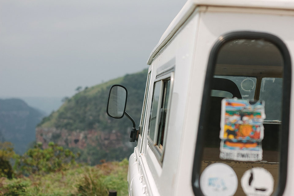 A photograph taken from directly behind a white vehicle as it travels on a wilderness landscape