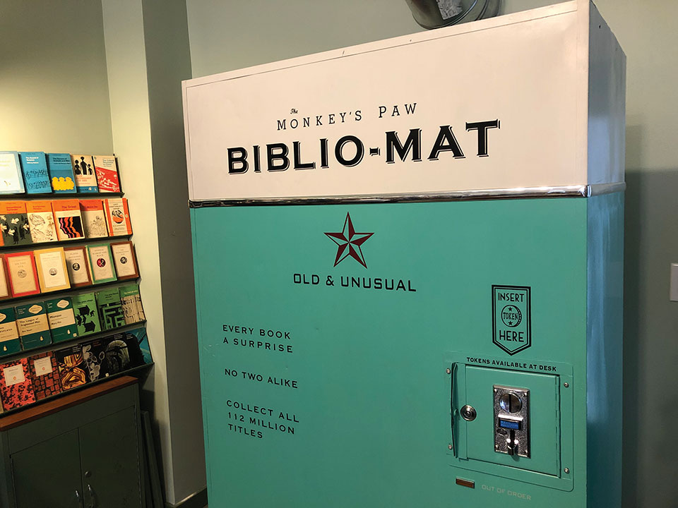 A vending machine. That visible text reads Monkey's Paw Biblio-Mat with the phrase Old & Unusual appearing half-way down the machine