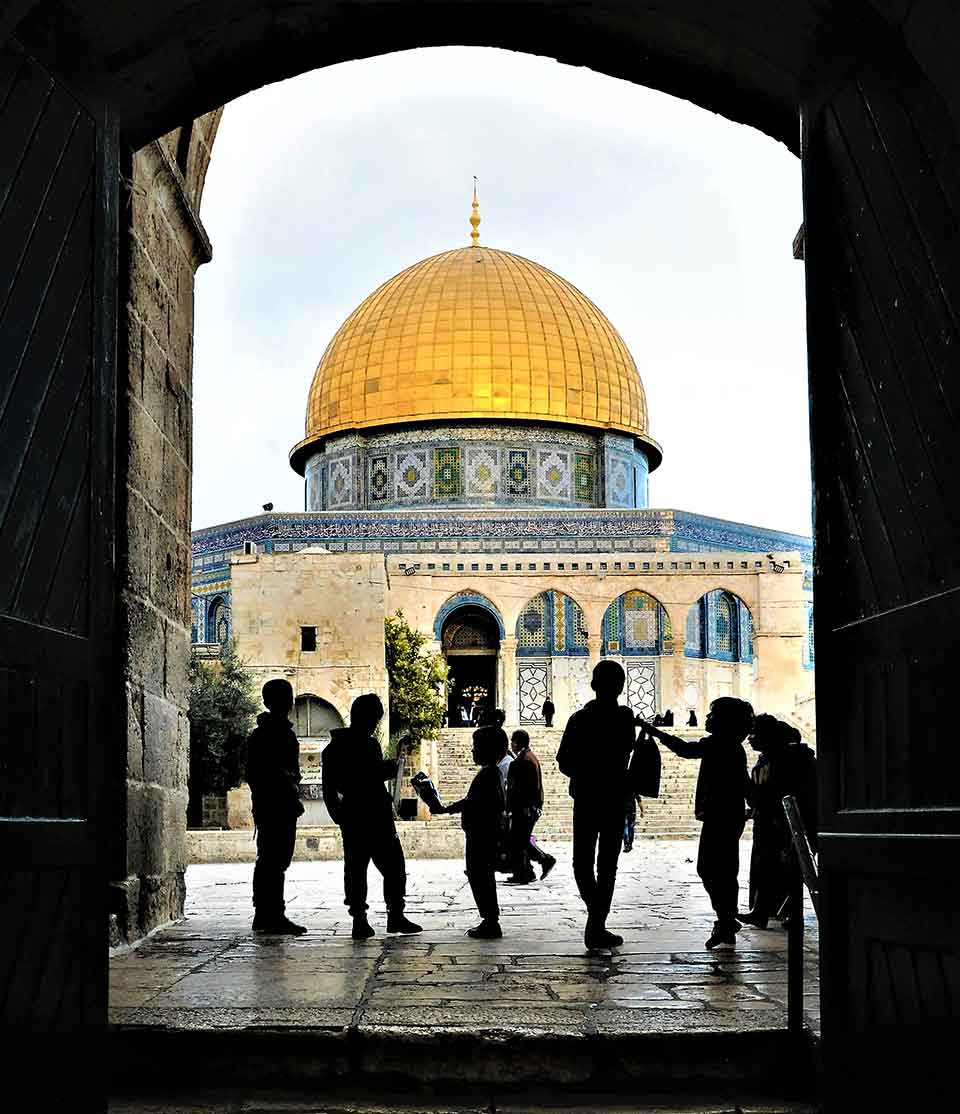 A photograph of children, bathed in shadow, gathered in an arch that faces the Dome of the Rock