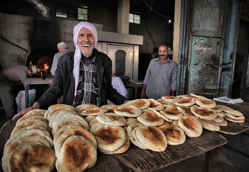 A photograph of two men, smiling at the camera, standing behind a table full of freshly baked bread