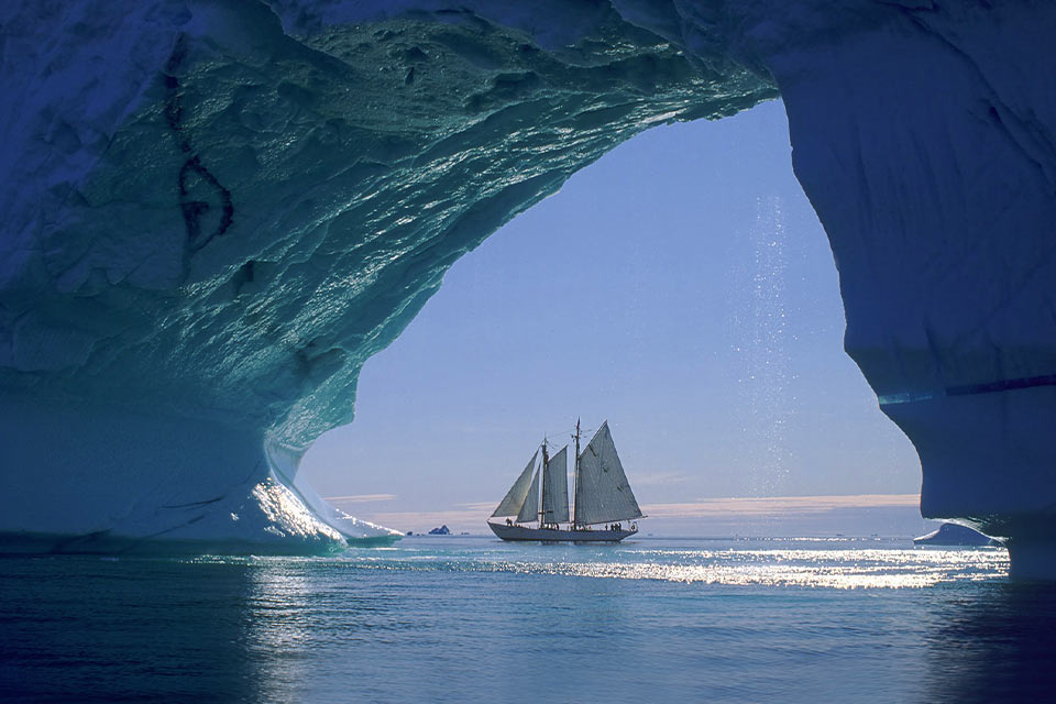 A photograph of a sail boat on the water as seen from inside of an icy cave