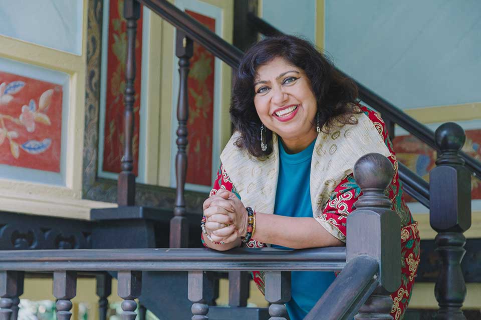 Dipika Mukherjee leans over a railing, smiling, as she looks at the camera