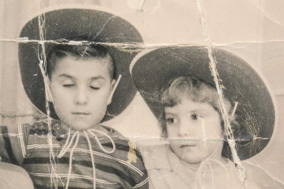 An old black and white photograph of a young boy and girl, both wearing cowboy hats, sitting next to one another