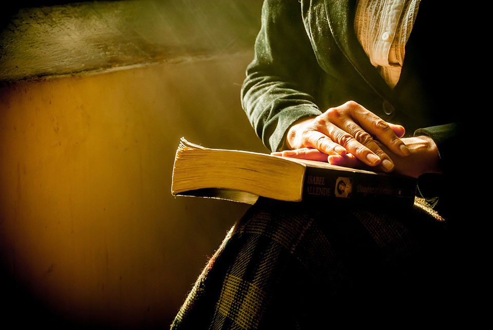 A close-up shot of a book resting in an unknown person's lap with light streaming in from the left