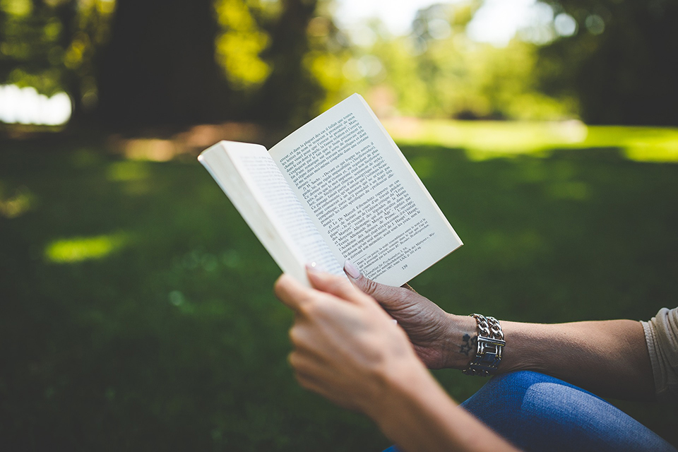 Person reading a book outside on green grass.