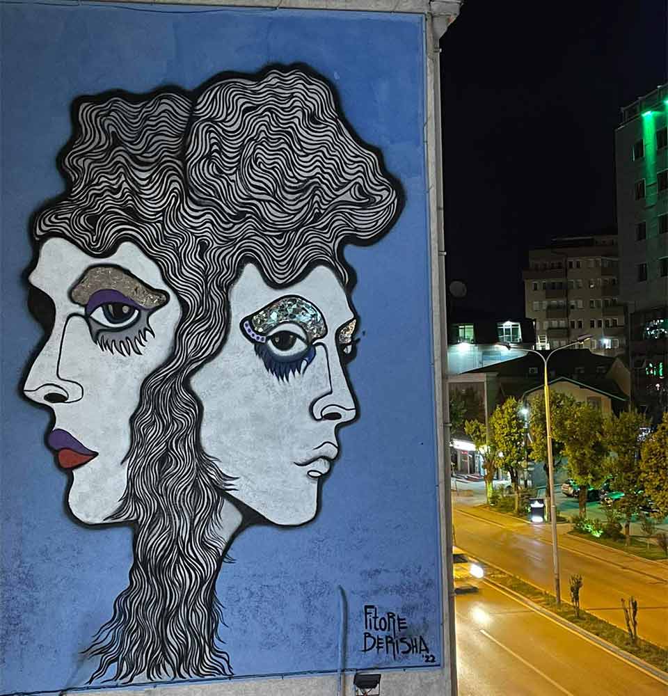 A photograph of a mural composed of two faces on a city street at night