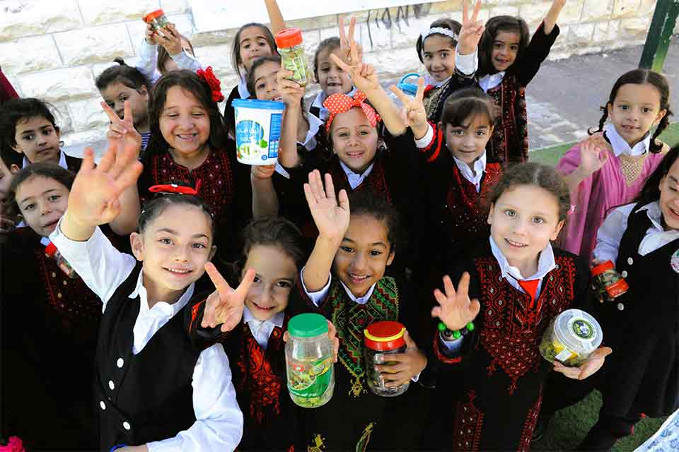 A photograph of Palestinian children in school uniforms smiling for the photographer, who is above them