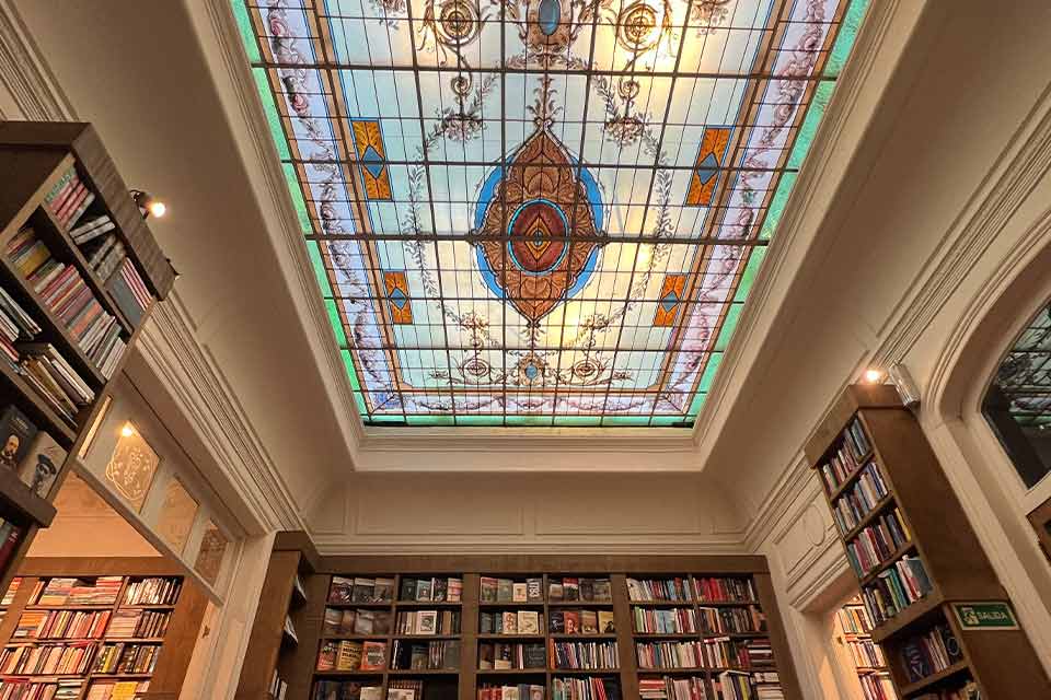 A photograph of the interior of Escaramuza looking up toward the intricate stained glass skylight