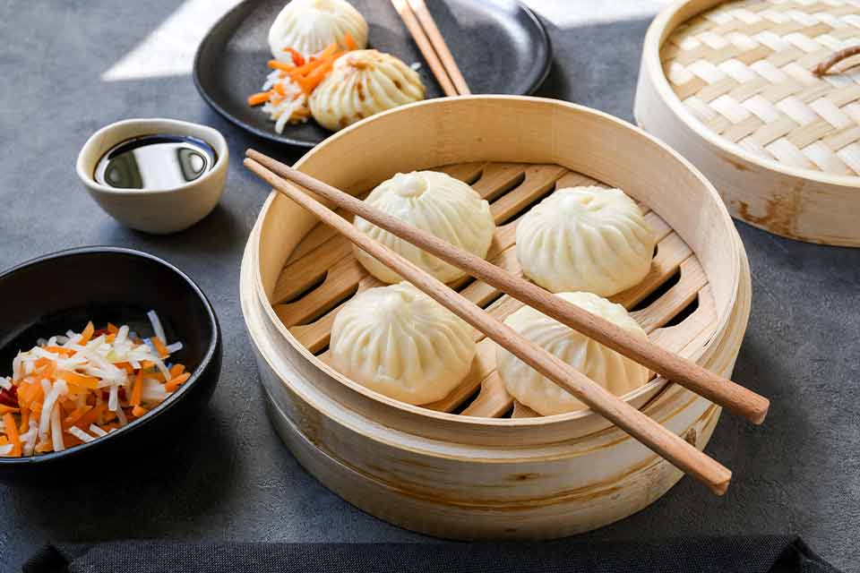 A photograph of steamed dumplings in a bamboo tray