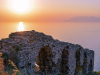 The remains of a stone arch perched on the edge of a cliff overlooking a sea