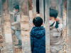 An image of two boys in a forest. Mirrors are placed so that one of the boys appears to be in several places at once.