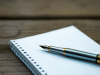 A fountain pen rests on a notebook of lined paper