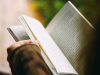 A girl reading a book and wearing a sweater.