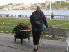 A photograph of an older woman standing by a bench, which is itself beside a river