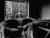 A black and white photograph of two chairs inside a home. Rubble has fallen on them, presumably from a bomb blast