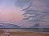 A beach dissolves into a shallow sea, beneath a purpled sky laced with wispy clouds