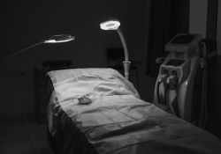 A photograph of a hospital bed bathed in light in a room swathed in shadow