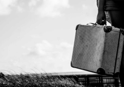 A black and white photograph of a hand attached to a figure in a business suit, holding a weathered suitcase