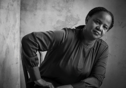 A black and white photo of Edwidge Danticat, seated but leaning forward slightly, with her hand on her leg